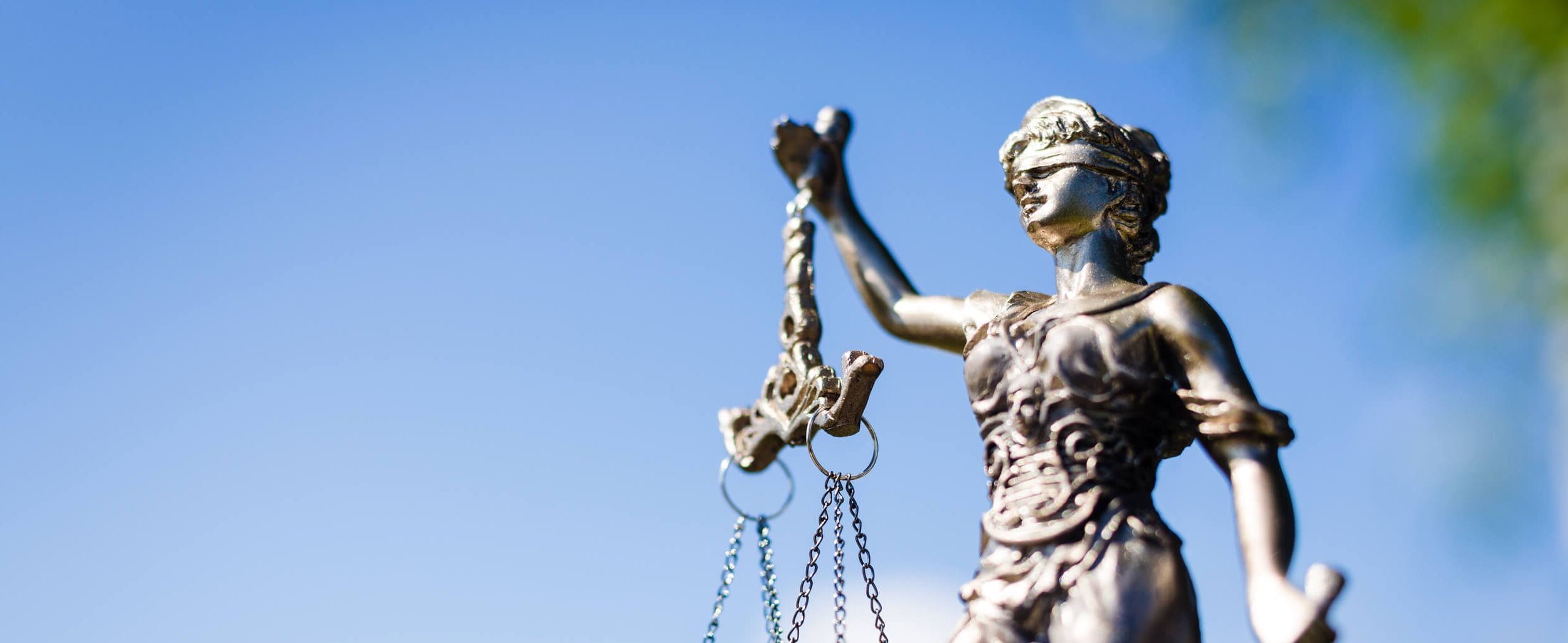Justitia-Statue mit Waage und Schwert vor blauem Himmel, Symbol für Gerechtigkeit und Rechtsstaatlichkeit